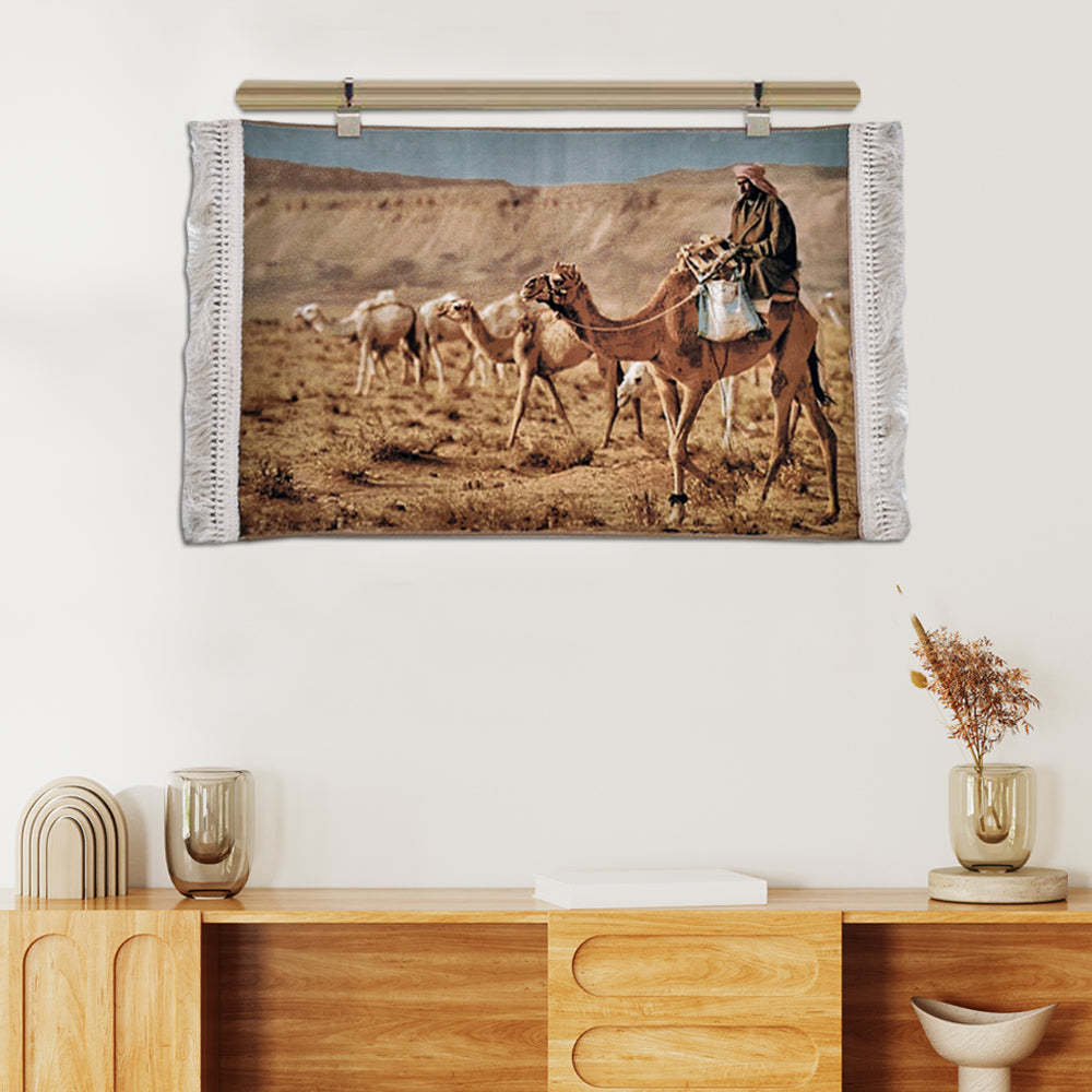 Wall tapestry depicting Bedouin man riding a camel across the desert with camel herd, in warm earthy tones